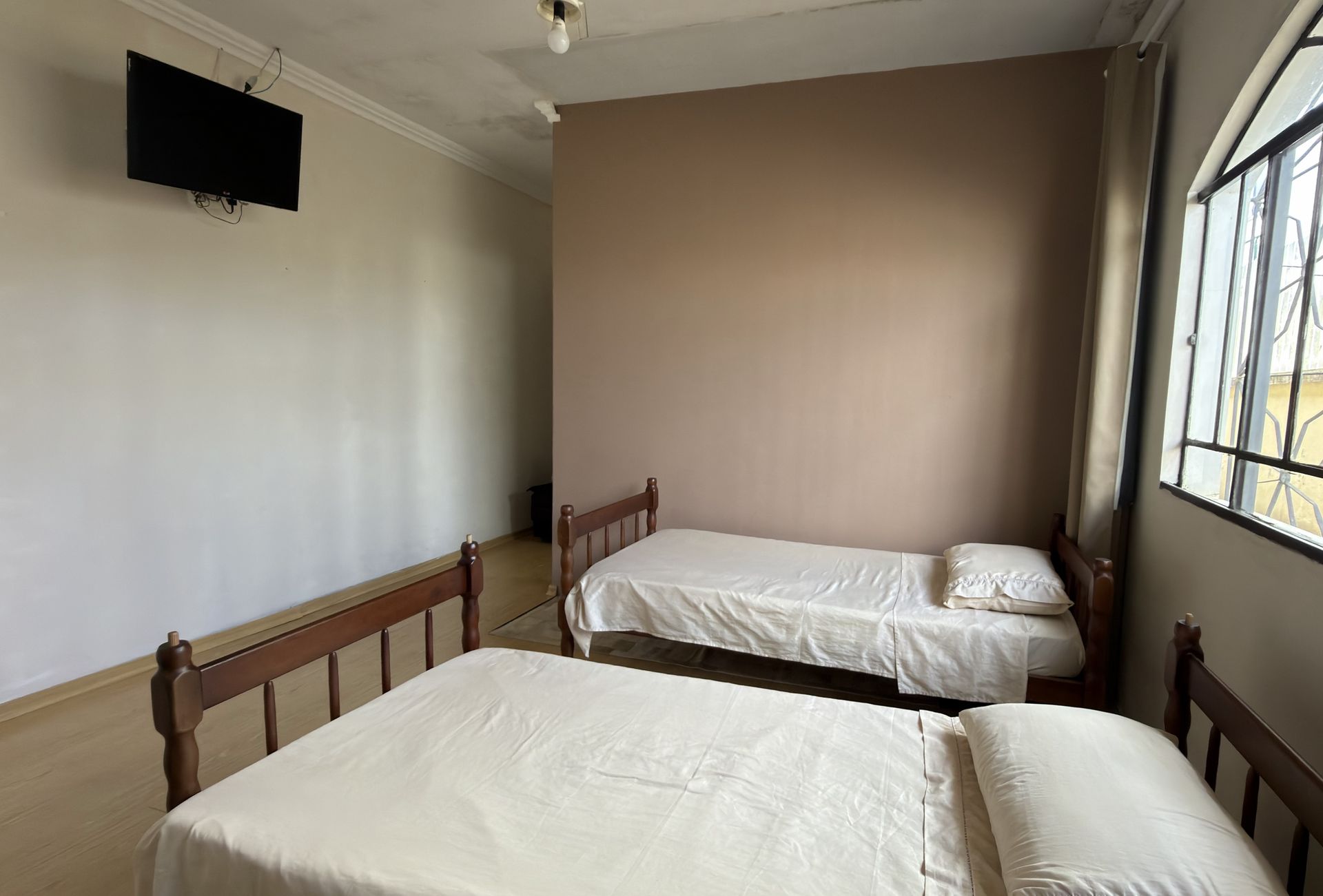 Suíte da casa com duas camas, TV na parede e janela em arco.