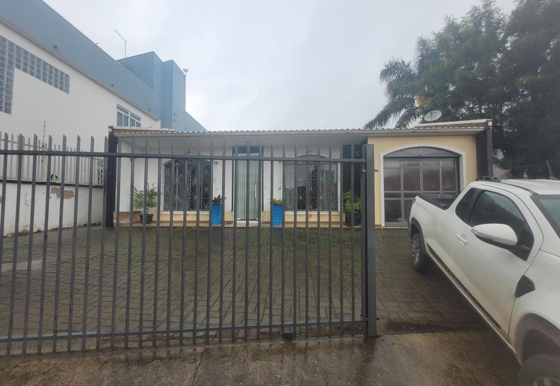A fachada da hospedagem, com o portão, o jardim e o estacionamento na frente.