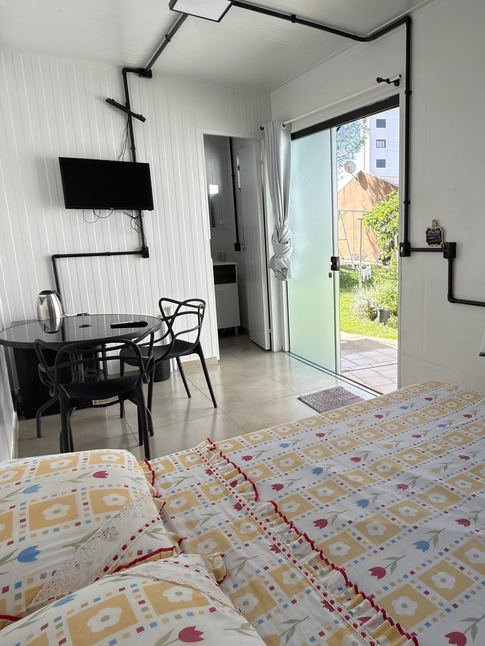 A cama de casal do Quarto 5, com colcha estampada, e a porta de vidro para o jardim.