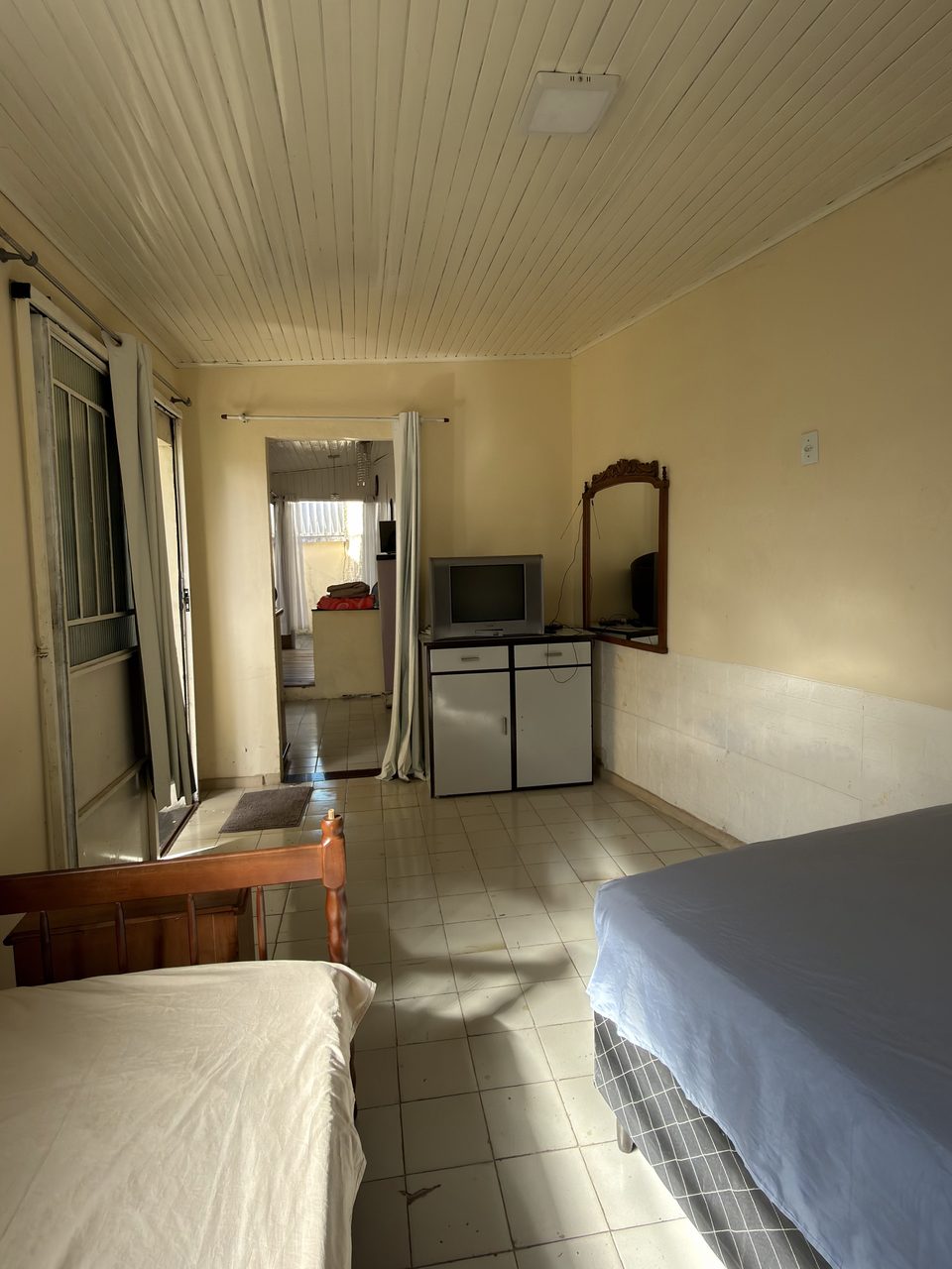 O Quarto 2 visto das camas até a porta, com a TV e o espelho.
