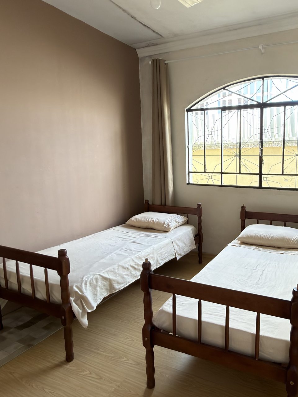 O Quarto 3: duas camas de solteiro de madeira embaixo da janela em arco, com o frigobar ao lado.